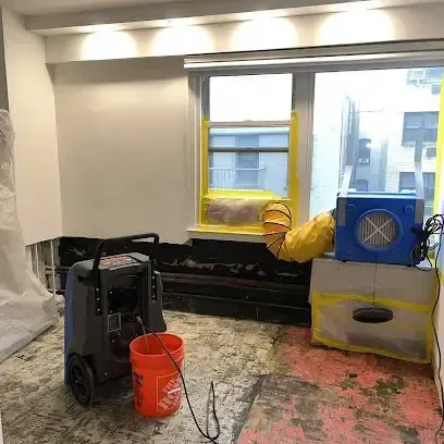 A dehumidifier and an air mover running in a room where the flooring was pulled up to dry the wet subfloor underneath