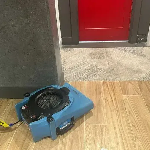 One air mover running over a wood-look tile floor beside an open doorway while the room dries out after water damage
