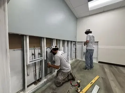 Two technicians cutting open a lower wall to reach supply pipes after a freeze