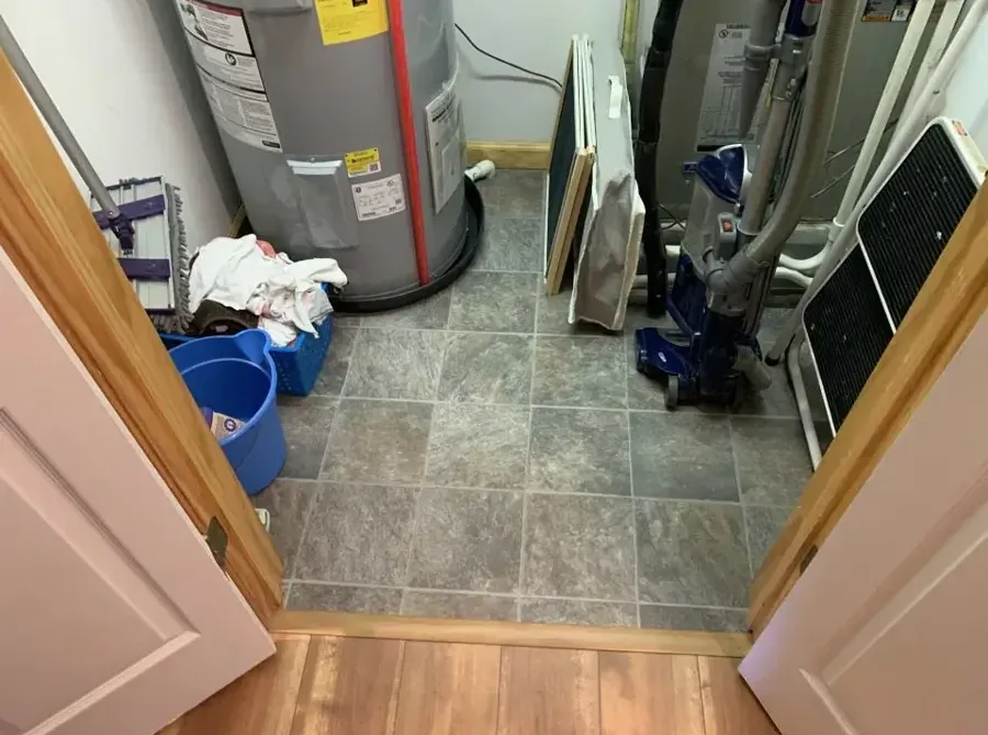 A water heater closet with towels and a bucket on the tile floor after a tank leak